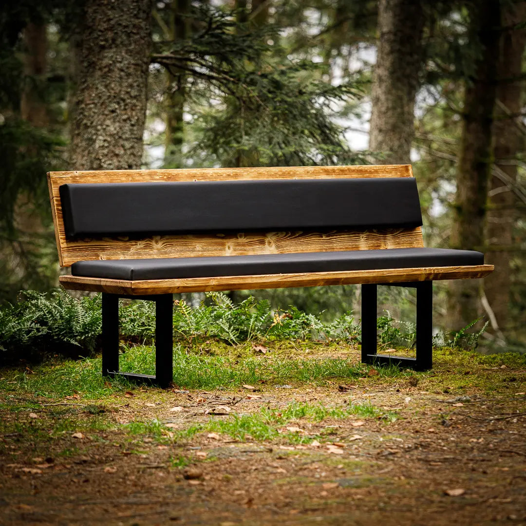 Geflammte Massivholz-Bank mit Rückenlehne und mit schwarzem Polster, die im Wald steht